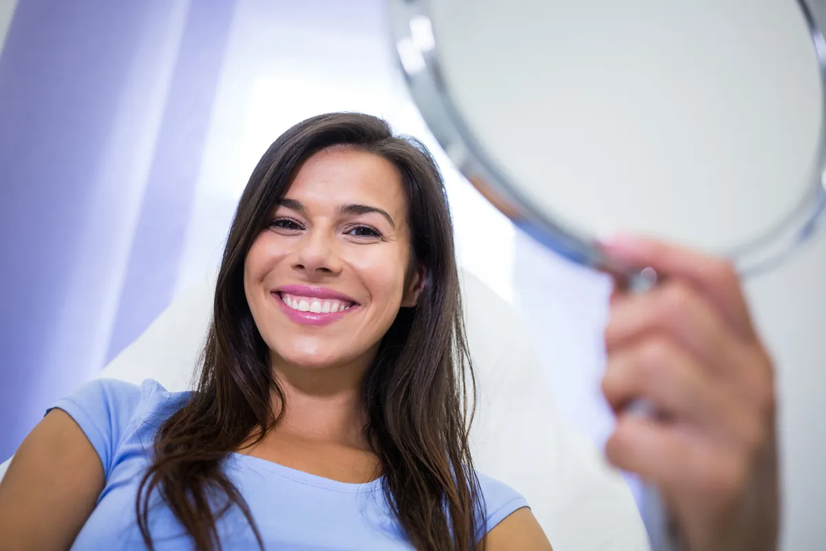 Paciente conferindo o sorriso no espelho após reabilitação com prótese dentária